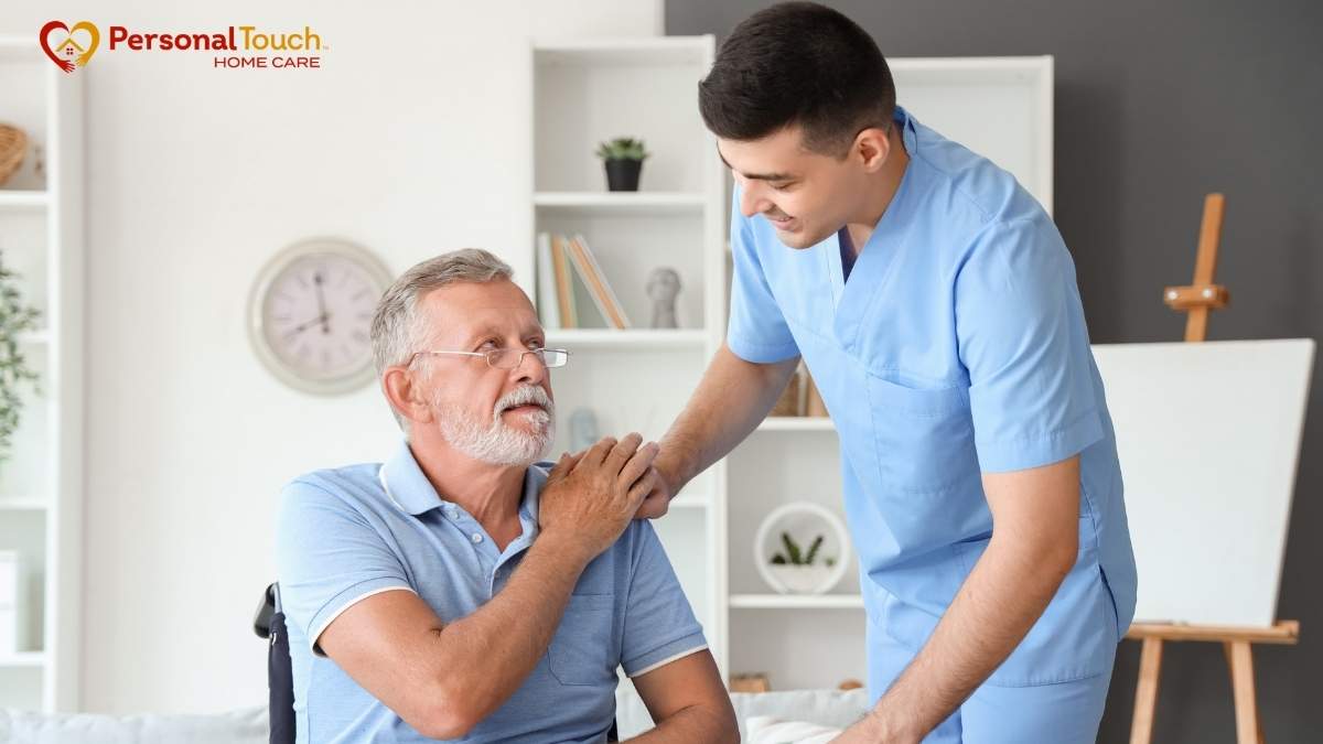 Male nurse assisting an elderly man in a wheelchair inside a home